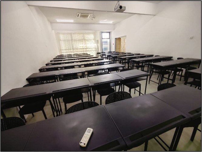 A refurbished classroom with rows of new black tables and chairs facing a projector screen