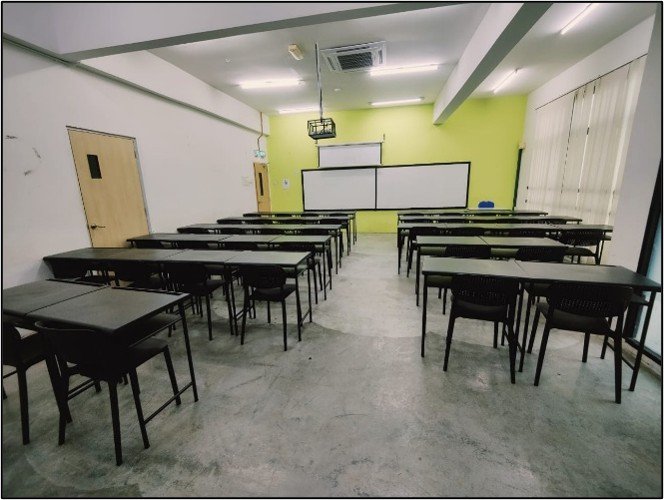 A refurbished classroom with new black tables and chairs, a whiteboard on a lime green wall, and a ceiling projector