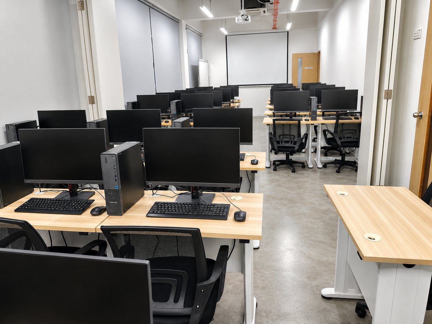 The new computer laboratory, with rows of monitors and desktop towers on light wood benches, mesh task chairs, a ceiling projector, and a pull-down screen