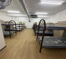 A larger hostel dormitory lined with bunk beds on new wood-effect flooring, with ceiling fans and air conditioning