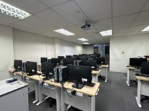 A computer lab with rows of new desktop computers on light wood benches, facing a ceiling-mounted projector