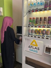 A student using an Atlas Oasis vending machine stocked with bottled drinks and canned beverages