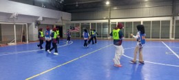 An indoor futsal match on a blue court, with players in green bibs