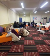 Students relaxing on orange sofas and at round tables in the refurbished student lounge, on a striped carpet