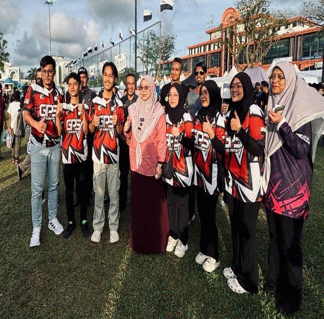Students in red and black team jerseys standing with staff at an outdoor community event