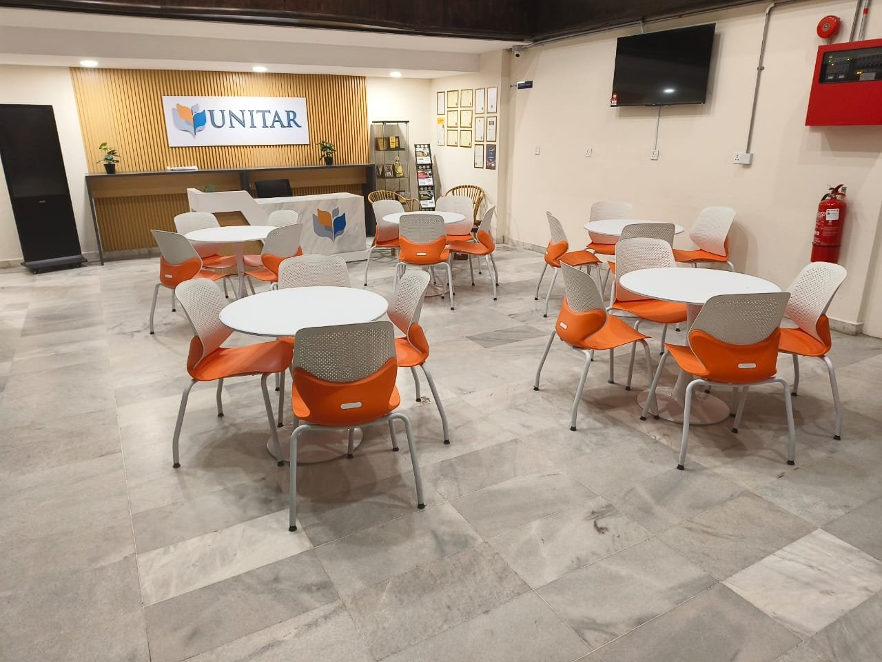 The refurbished campus reception area, with round white tables and orange chairs in front of a timber-slatted wall carrying the UNITAR sign