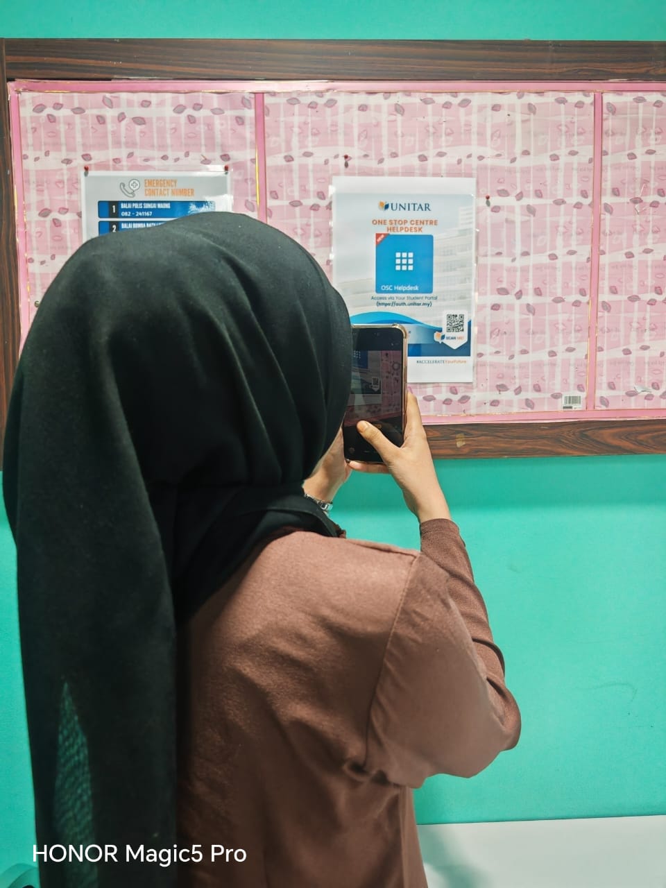 A student photographing the One Stop Centre Helpdesk poster pinned to a campus noticeboard