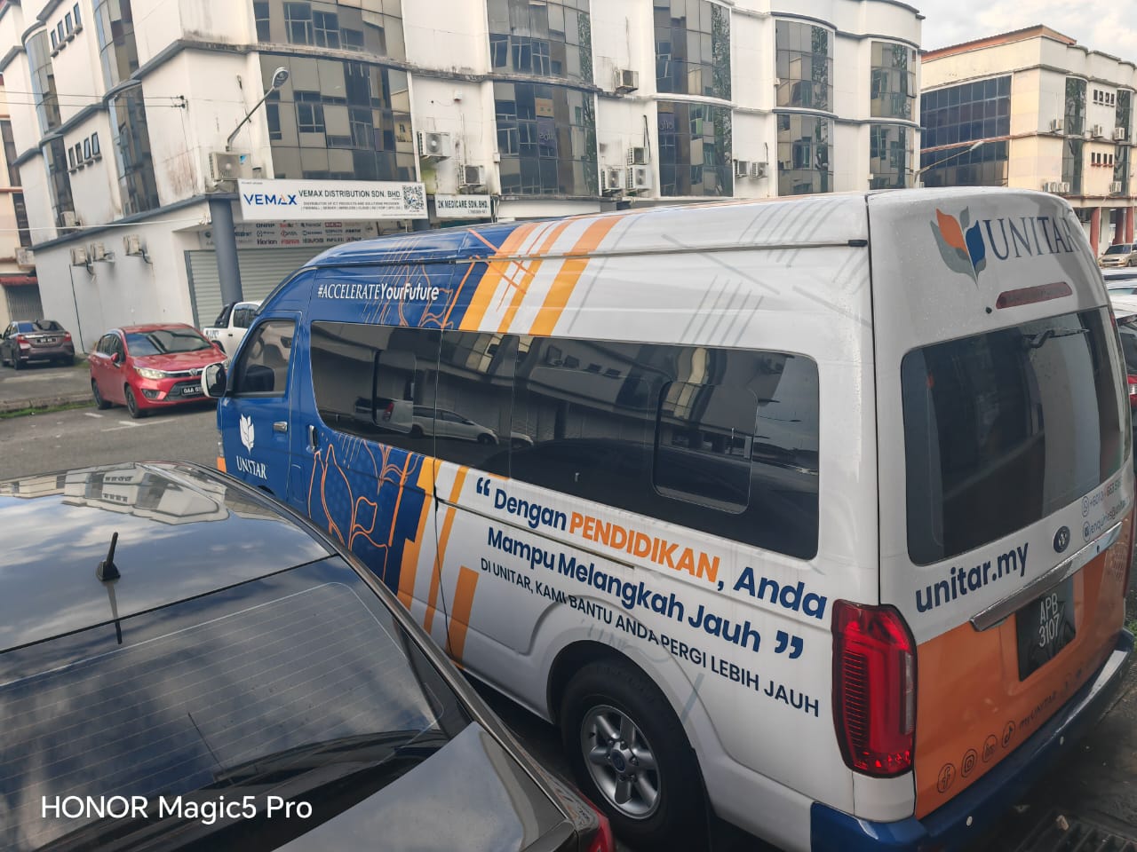 The UNITAR shuttle van parked on a street, branded with the UNITAR logo and the tagline Dengan Pendidikan, Anda Mampu Melangkah Jauh