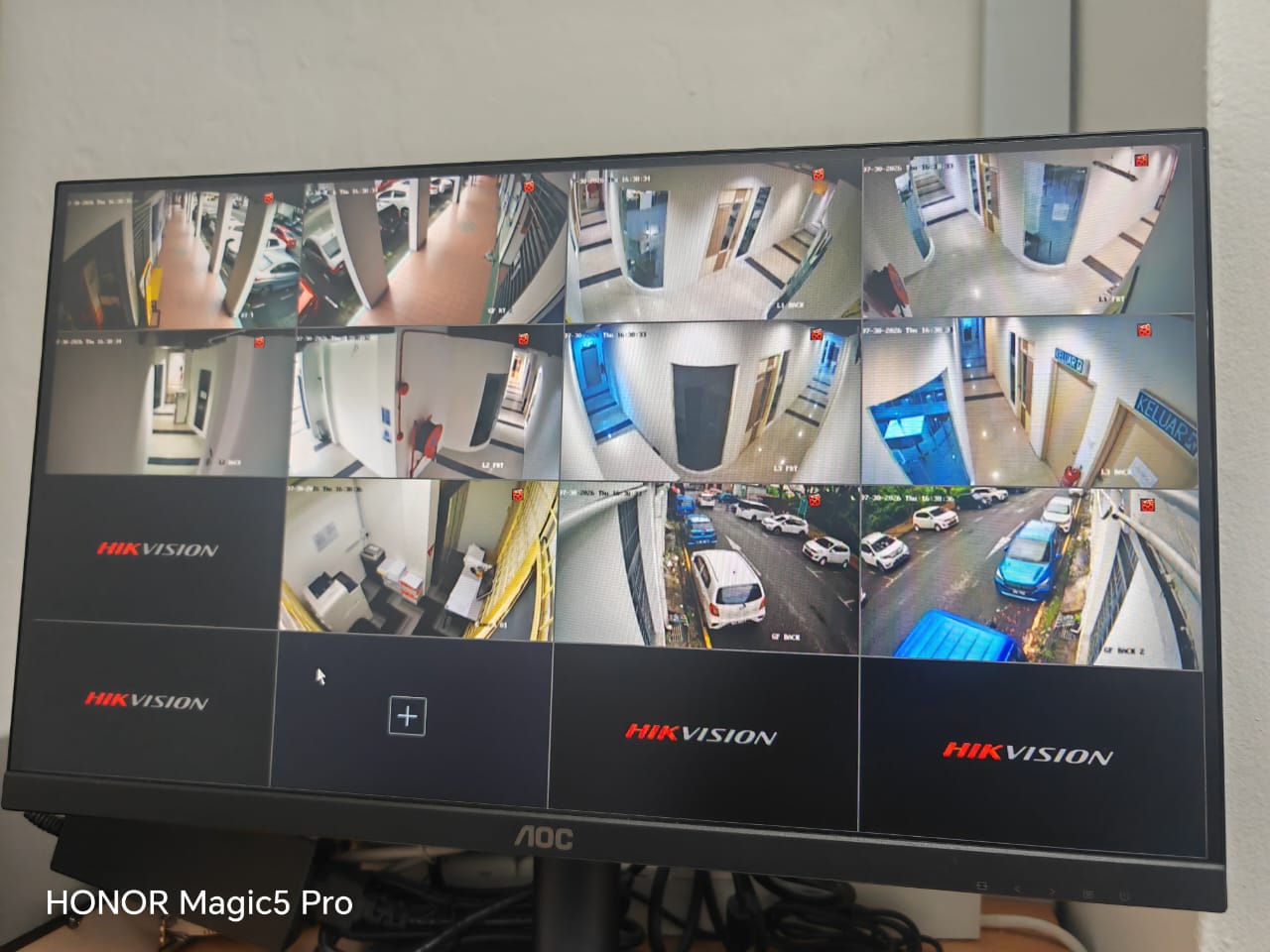 A security monitor displaying a grid of Hikvision CCTV camera feeds covering corridors, stairwells, and the road outside campus