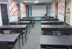 A refurbished classroom with new black study tables and chairs, facing a whiteboard and projector screen