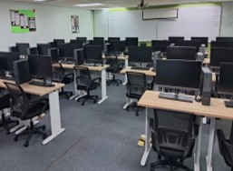 A computer lab with rows of new desktop computers on wood-effect benches