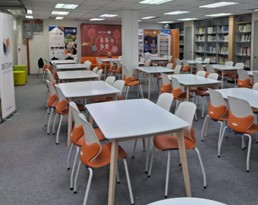The library with new white tables and orange chairs, beside shelving and a display board