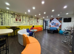 The student lounge with an orange sofa and low tables against a mural wall reading 'Believe in yourself, play hard, never give up'