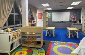 A second view of the Early Childhood Education lab, with a cot, low tables and chairs, a whiteboard, and a play kitchen