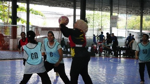 Students playing netball on an outdoor court, wearing position bibs