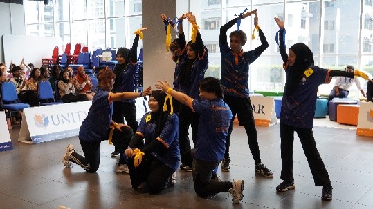 A team performing a synchronised aerobics routine in front of UNITAR banners