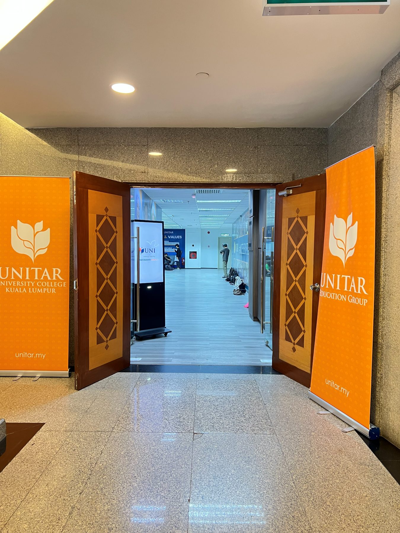 Open double doors leading into the Level 2 campus, flanked by tall orange UNITAR University College Kuala Lumpur banners