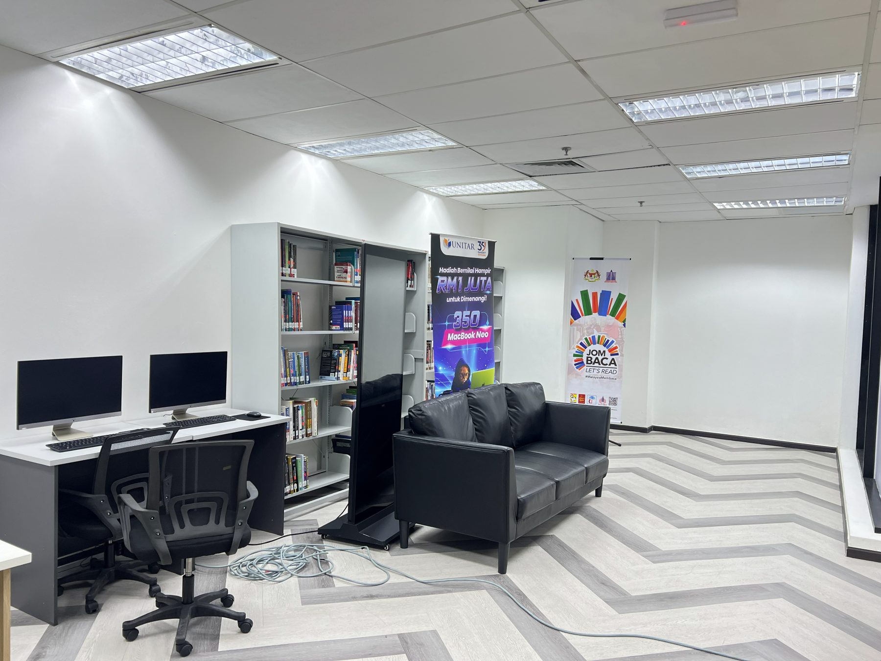 A mini library with book shelving, two desktop workstations along the wall, and a black sofa