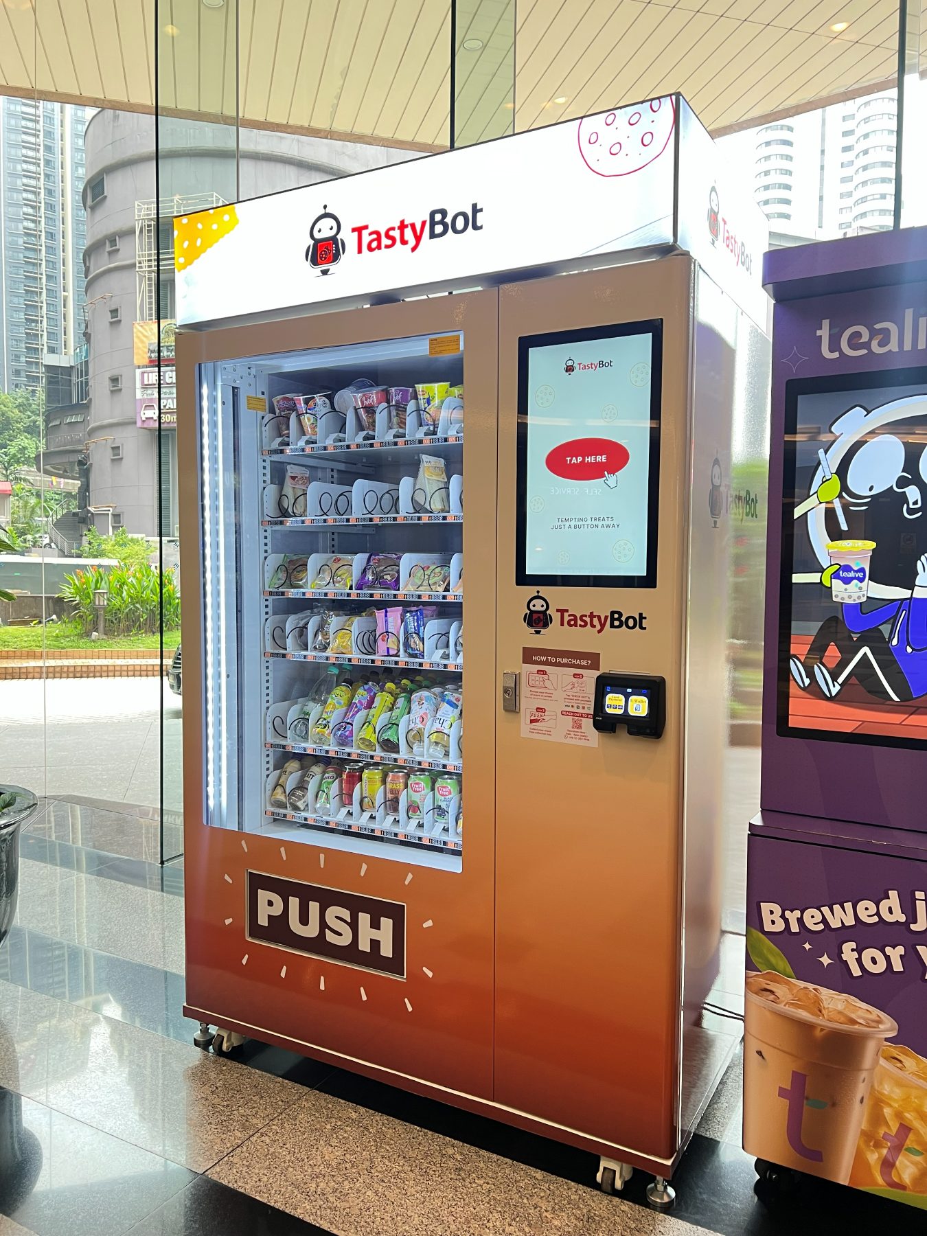 A TastyBot vending machine in the lobby, stocked with snacks and canned drinks, with a touchscreen and card reader on the right